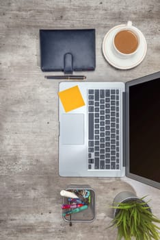 Top view of business desk with laptop, sticky notes, coffee, potted plant, notebook and business accessories on the office