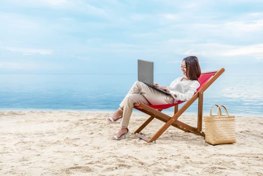 Asian business woman working with laptop sitting in the beach chair on beach. Summer vacation