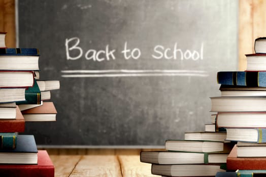 Close up view of pile of books on wooden table and blackboard with Back to School message. Back to School concept