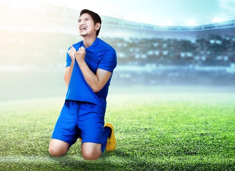 Asian football player man celebrate the goal with holding his jersey and kneeling on the football field at stadium