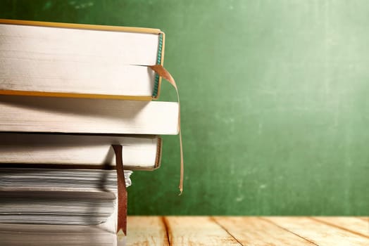 Close up view of pile of books on wooden table with chalkboard background. Back to School concept