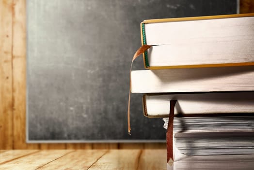 Close up view of pile of books on wooden table with blackboard background. Back to School concept