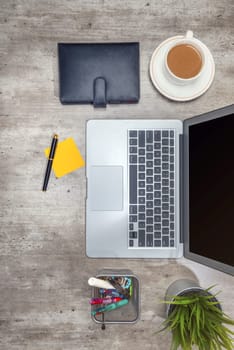 Top view of business desk with laptop, sticky notes, coffee, potted plant, notebook and business accessories on the office