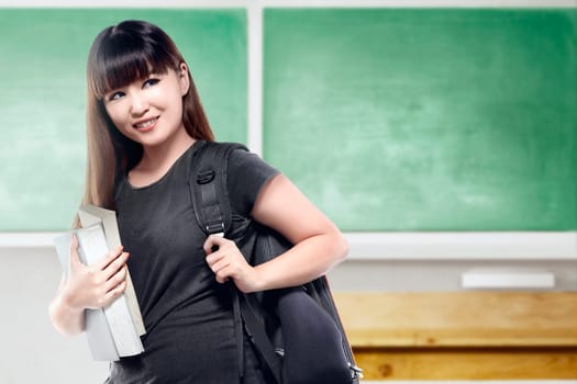 Asian student woman with backpack carrying book in the classroom with chalkboard background. Back to School concept