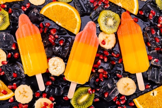 Fruit ice cream on stick with slices fruits on black slate board. Focus on Popsicles.