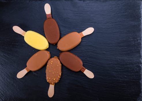 Ice cream on stick covered with chocolate on black stone slate board.