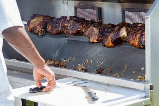 Barbecue  mobile spit cooking beef meat food on spindle with serving catering utensils outdoors food craft market.