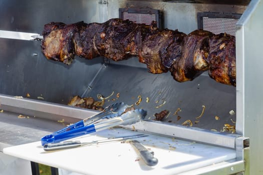 Barbecue  mobile spit cooking beef meat food on spindle with serving catering utensils outdoors food craft market.