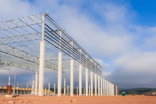 Building new large warehouse construction building structure halfway concrete columns steel roofing beams.