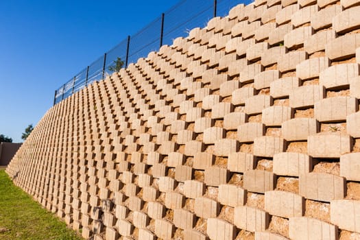 Wall retaining blocks inter locking concrete products closeup structure construction with fencing on field plateau.