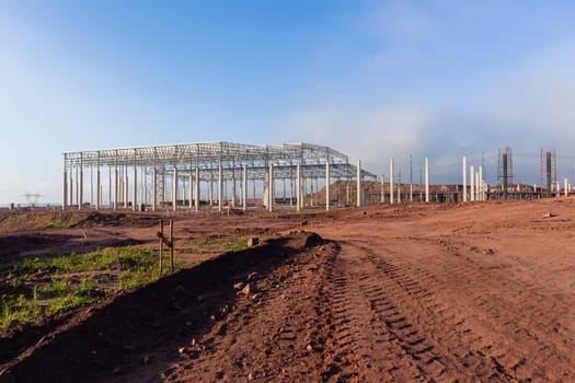 Building new large warehouse structure construction halfway concrete columns steel roofing beams.