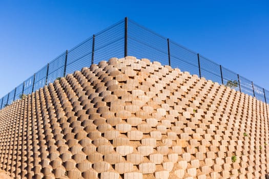 Wall retaining blocks inter locking concrete products closeup structure construction with fencing on field plateau.