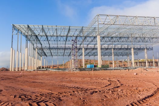 Building new large warehouse structure construction halfway concrete columns steel roofing beams.