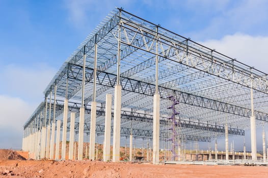 Building new large warehouse structure construction halfway concrete columns steel roofing beams.