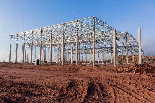 Building new large warehouse structure construction halfway concrete columns steel roofing beams.