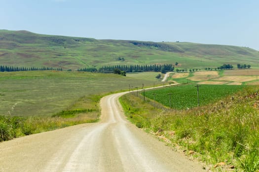 Dirt road route through farmlands fields crops hills scenic rural mountain summer terrain.