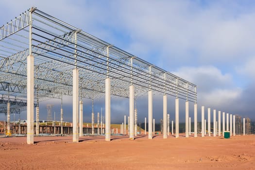 Building new large warehouse construction building structure halfway concrete columns steel roofing beams.