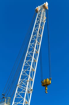 Crane arm rigging lifting machine with cables dual pulleys to hoist hook against blue sky.
