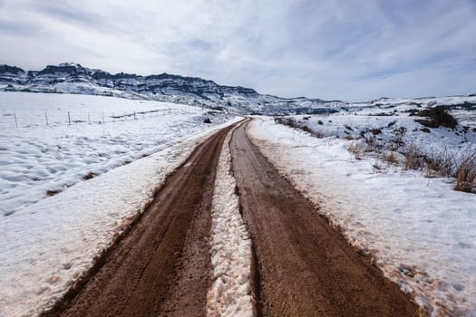Mountains Snow dirt road vehicle tracks towards hilltop in winter landscape