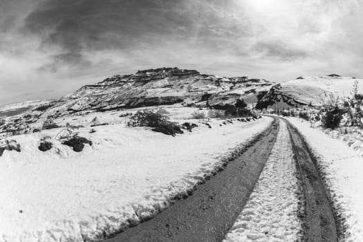 Mountains Snow dirt road tracks towards hilltop in vintage black and white landscape