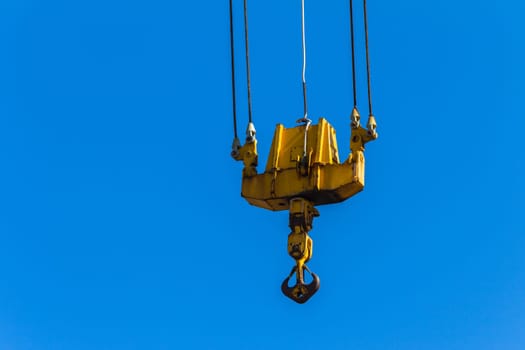 Crane lifting hook with cables dual pulleys closeup against blue sky..