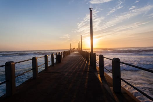 Beach pier jetty railing platform overlooking ocean waters horizon morning blue sky landscape.