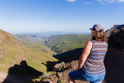 Woman closeup rear photo adventurer looks over mountains deep valley dirt road pass landscape summer afternoon.