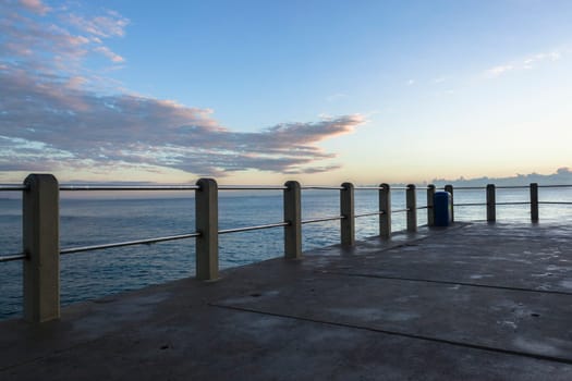 Beach pier jetty railing platform overlooking ocean waters horizon morning blue sky landscape.