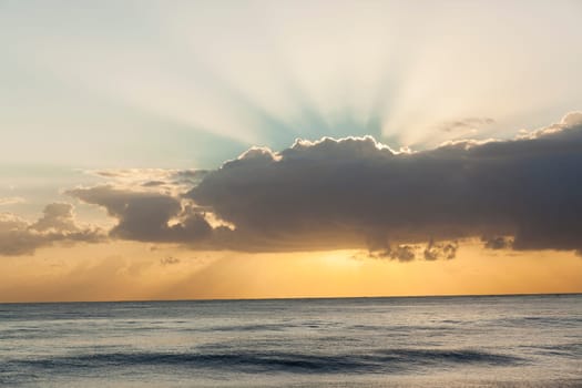 Ocean waters horizon sunrise light rays behind clouds scenic nature landscape.