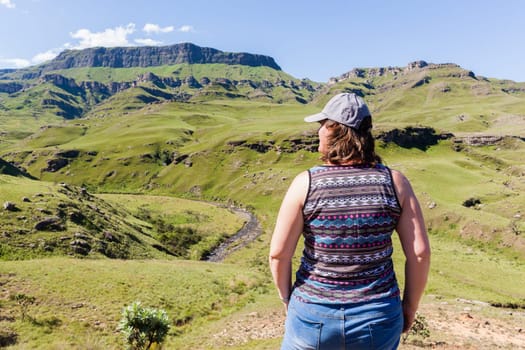 Woman closeup rear photo adventurer looks over mountains deep valley dirt road pass landscape summer afternoon.