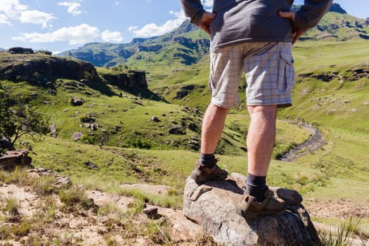 Hiker closeup rear from legs of adventurer looking over mountains  valley river on Sani-Pass landscape summer afternoon.