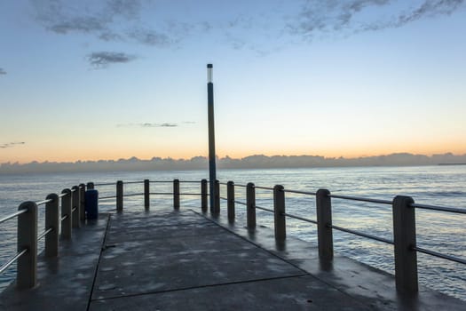 Beach pier jetty railing platform overlooking ocean waters horizon morning blue sky landscape.