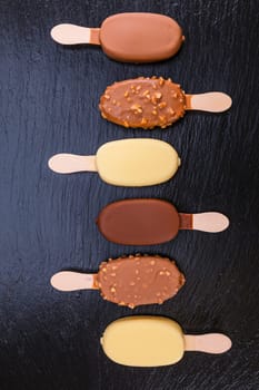 Ice cream on stick covered with chocolate on black stone slate board.