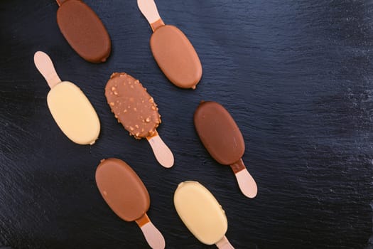 Ice cream on stick covered with chocolate on black stone slate board.
