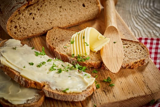 Buttered slices of fresh rye bread topped with chopped parsley and a decorative twist or curl of butter on a wooden board with spreader or butter knife
