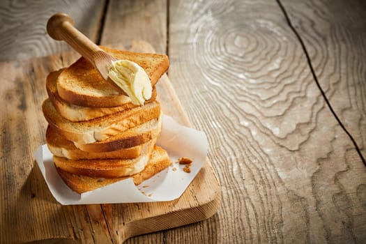 Toasted fresh white bread stacked into a tower topped with a wooden spreader or butter knife on a rustic table with copy space and woodgrain texture
