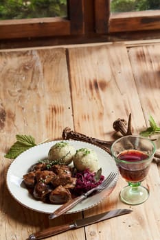 Wild venison goulash in a rich gravy served with a glass of red wine on a table decorated with deer antlers with copy space