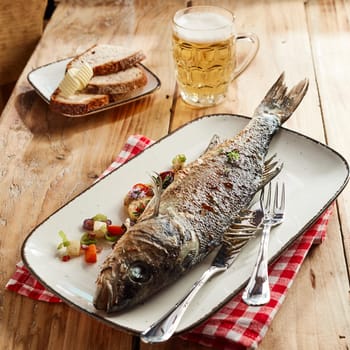 Delicious pub lunch with whole grilled sea bass served on a platter with a tankard of cold frothy beer and rye bread with butter