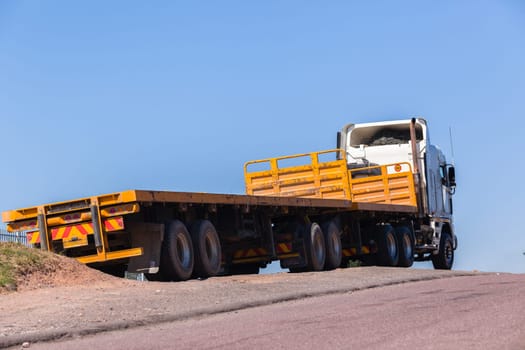 Truck with yellow haulage trailers awaiting cargo parked outside blue sky day.