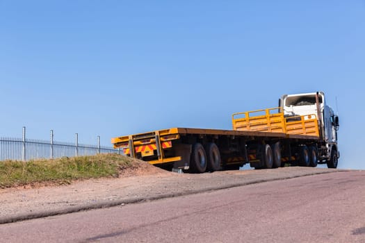 Truck with yellow haulage trailers awaiting cargo parked outside blue sky day.