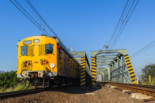 Train passenger coaches closeup on rail tracks crossing bridge to city countryside.
