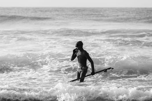 Spearfishing unidentified diver on beach about to enter blue ocean sea waters swimming sporting lifestyle