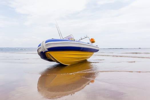 Fishing inflatable boat fiber-glass hull outboard motors craft on beach sands at water edge.