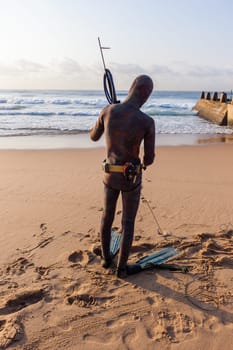 Spearfishing unidentified diver on beach about to enter blue ocean sea waters swimming sporting lifestyle