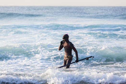 Spearfishing unidentified diver on beach about to enter blue ocean sea waters swimming sporting lifestyle