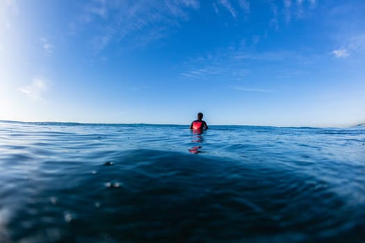 Surfer surfing sitting waiting ocean waves on blue horizon water photo.