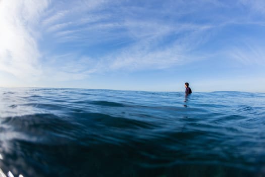 Surfer surfing sitting waiting ocean waves on blue horizon water photo.