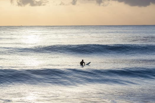 Surfer in ocean silhouetted waiting for waves early morning sunrise surfing session.