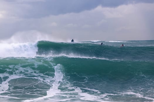 Surfers surfing out in large ocean storm waves.