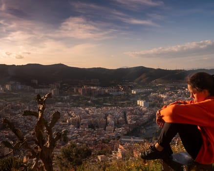 Sad girl sitting on the hill embracing her knees and looking away at sunset, sadly depressed teenager spending time alone, thoughtful young girl feeling lonely or frustrated thinking about problems